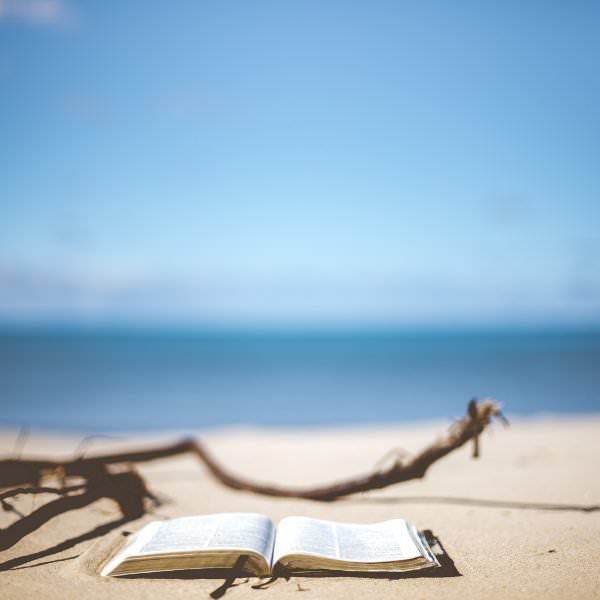 Open book on sandy beach - what to read while you're on holiday