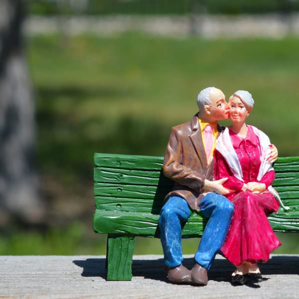 Senior couple sitting on park bench, kissing (models)